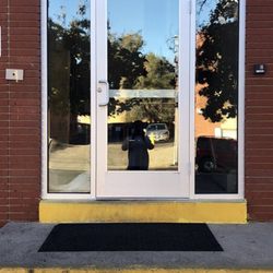 All About Glass of Colorado - A new commercial aluminum-framed glass door and side-lites are installed in a red brick wall above a yellow painted step...