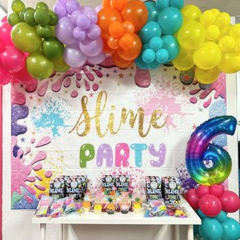 Slime World - A birthday party setup with balloon clusters in various colors, a slime-themed backdrop, and a table with party favors and cupcakes for a child's sixth birthday. - Party & Event Planning Near Me - Fairfield, California