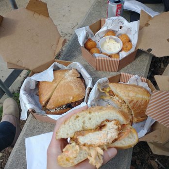 Grégoire - Holding half the fried buttermilk chicken filet with spicy cole slaw on French roll - French Near Me - Berkeley, California