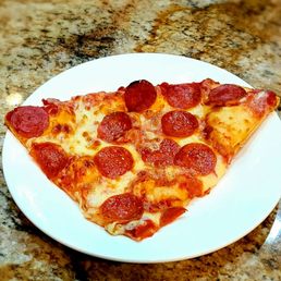 Thin crust Pizza - A slice of pepperoni pizza with melted cheese, pepperoni slices, and a golden crust is placed on a white round plate. The plate rests on a speckled granite countertop, and the pizza appears freshly baked with a crispy crust and evenly distributed toppings.