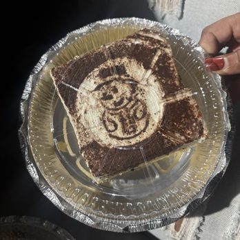 La Catrina - Tres Leche Sponge Cake - A slice of Tres Leche Sponge Cake with chocolate topping is on a clear plastic plate, held by a person with painted nails. - Mexican Near Me - Newburgh, Indiana