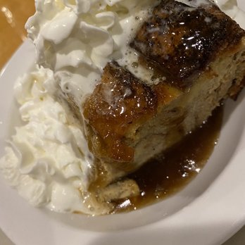 Narrows Crossing Restaurant - Bread pudding - A piece of bread pudding with caramel glaze is served with whipped cream on a white plate, featuring a water view in the background. - Seafood Near Me - Wareham, Massachusetts