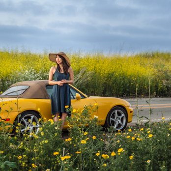 Embrace Photos - A woman in a sunhat poses in front of her yellow Miata in front of a field of yellow flowers. - Session Photography Near Me Embrace Photos - A woman in a sunhat poses in front of her yellow Miata in front of a field of yellow flowers. - Session Photography Near Me