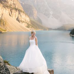 Geoff Wilkings Photography - Bride standing on rocks at Moraine Lake in Banff National Park with the Valley of the Ten Peaks in the background, holding and adjusting her