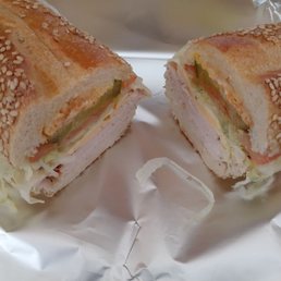 Wasn't it Keats who said, "a thing of beauty is a joy forever"? i could stare at this sandwich all day - such a fond, delicious memory - A sandwich cut in half reveals layers of lettuce, tomato, deli meat, and bread with sesame seeds on top, placed on aluminum foil.