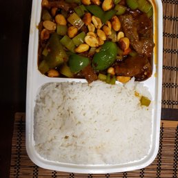 Crab Rangoon 蟹角 - The image shows a plastic take-out container with two compartments. One compartment contains white rice, and the other contains beef with vegetables in a dark sauce, including green bell peppers, celery, and peanuts. The container is placed on a bamboo mat, and the meal appears to be a Chinese or Asian-inspired dish.