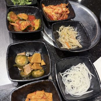 Ohgane - Banchan. Fav is the pickled onion and jalapeno - A collection of small black bowls containing Korean banchan, including pickled cucumbers, kimchi, and other vegetables, arranged on a black table. - Korean Near Me - Concord, California