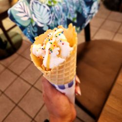 Coconut ice cream with pineapple in a cone with Carmel and sprinkles on top.