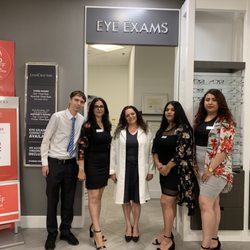 Doctor and friendly staff standing in front of the exam entrance and hours.