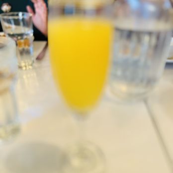 Maharaja - A glass of orange juice is in focus on a table at a restaurant, with other glasses and people in the background. - Indian Near Me - Milwaukee, Wisconsin