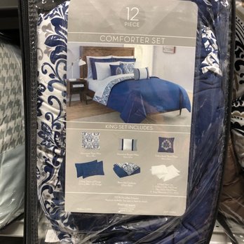 Gabe's - The image shows a packaged 12-piece comforter set with a bedroom scene on the label. The bedding features a blue and white color scheme, with pillows, a comforter, and decorative accents. The packaging is clear plastic, revealing the fabric pattern and color. The label details the included items such as pillows, shams, and comforter, and indicates the set is made of 100% microfiber. The scene suggests a bedroom setup, with a wooden headboard and side table visible in the background. - Discount Store Near Me - Buffalo, New York