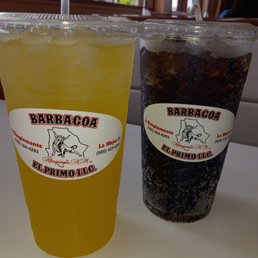 The pineapple horchata is so refreshing. - Two beverages in clear plastic cups with straws are placed on a white surface. One drink is yellow, and the other is dark with bubbles. Both cups have a label from Barbacoa El Primo LLC in Albuquerque, NM.
