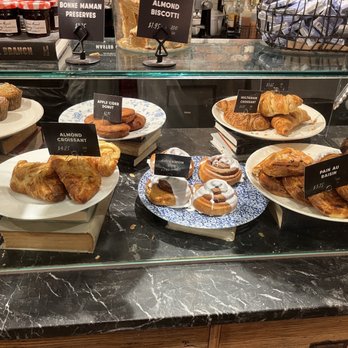Caffe Nero - Baked goodies 10/17/22 - Assorted baked items such as almond croissants, cinnamon buns, apple cider donuts, and muffins are arranged on plates inside a bakery display case. - Coffee & Tea Near Me - Boston, Massachusetts