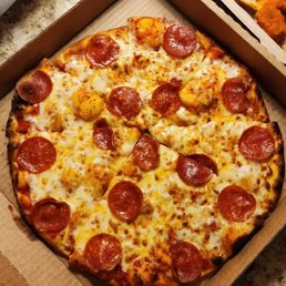A pepperoni and cheese pizza in a cardboard delivery box on a granite countertop, with a side of fried chicken and a small drink nearby.