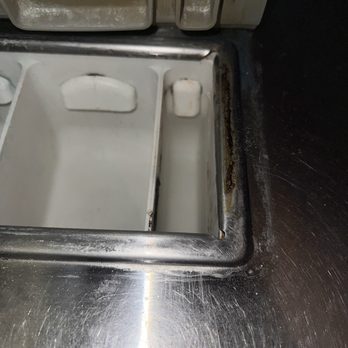 Breeze Laundry - Yuck - A stainless steel laundry machine with rust and dirt buildup around the edges, showing signs of wear and lack of cleaning. - Laundry Services Near Me - Springfield, Missouri