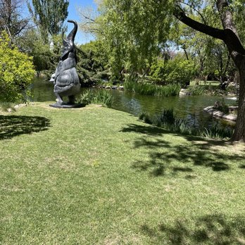 Nedra Matteucci Galleries - The garden behind the gallery - A garden scene featuring a large elephant sculpture with a bird on its back near a pond, surrounded by trees and greenery. - Art Galleries Near Me - Santa Fe, New Mexico