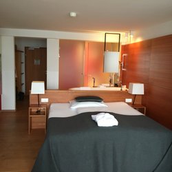 Seehotel Grundlsee - Blick vom Fenster (Arbeitsplatz) is Zimmer. Bett, dahinter die frei stehende Badewanne und versteckt hinter den Türen Dusche und WC