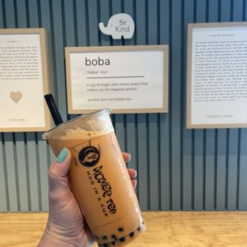 Kokee Tea - Thai Milk Tea with bobas foregrounding an interior wall that features art (defining boba) and a sign that encourages readers to "be kind." - Bubble Tea Near Me - Lorton, Virginia