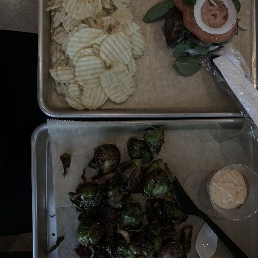two trays of food including a sandwich, chips, and brussels sprouts