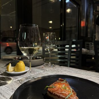 Marson Caffè - Fried saganaki - Fried saganaki cheese is presented on a black plate at a restaurant table, accompanied by two glasses of white wine and a lemon wedge. - Cafes Near Me - Brooklyn, New York