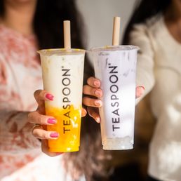 Silky Mango W/ Boba - Two women hold large bubble tea drinks with the TEA AS POON logo, one with a yellow and white drink, the other with a purple and white drink.
