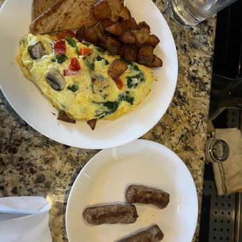 Vine Bistro - A breakfast meal featuring scrambled eggs with vegetables, two slices of toasted bread, roasted potatoes, and three sausage links on a white plate, with a glass of water nearby. - Wine Bars Near Me - Ormond Beach, Florida