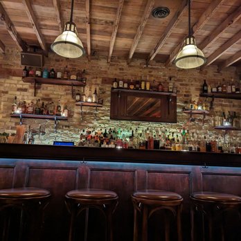 The Meadowlark - A bar with a brick wall, wooden shelves filled with liquor bottles, and hanging pendant lights illuminating the space. - Speakeasies Near Me - Chicago, Illinois