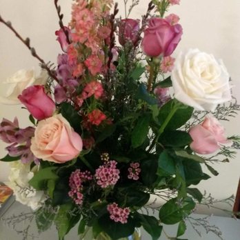Periwinkle Florist - A bouquet of mixed flowers including roses, small pink flowers, and greenery in a glass vase, placed on a table. - Florists Near Me - Cary, Illinois