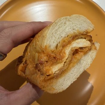 Deep End Subs - Chicken Parm - A person holds a chicken parm sandwich with breaded chicken, marinara sauce, and cheese, on white bread, over an orange plate. - Sandwiches Near Me - Austin, Texas