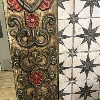 Range Cafe - The image features a vertically oriented carved wooden panel with intricate floral and scroll motifs painted in red and green, showing signs of aging and wear. To the right of the panel, there are tiles with a geometric star pattern in black and white. The setting appears to be indoors, with a wooden floor visible at the bottom left corner. - Breakfast & Brunch Near Me - Albuquerque, New Mexico