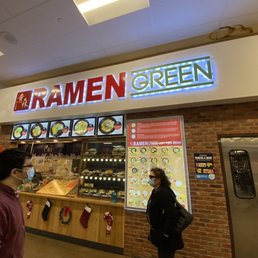 a man and a woman standing in front of a ramen green a man and a woman standing in front of a ramen green