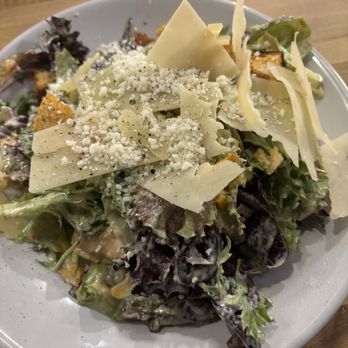 M’tucci’s Bar Roma - Caesar salad - A Caesar salad with leafy greens, cheese shavings, croutons, and grated cheese served on a white plate at a restaurant. - Cocktail Bars Near Me - Albuquerque, New Mexico