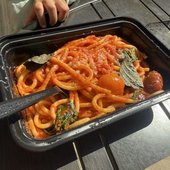 ZaVino - Pasta pomodoro - A black plastic container holds pasta pomodoro with tomato sauce, cherry tomatoes, and basil leaves, placed on a wooden table. - Italian Near Me - Baltimore, Maryland