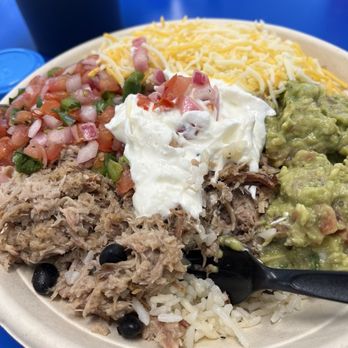 From the Wildfire - A disposable plate contains shredded meat with black beans, white rice, guacamole, sour cream, shredded cheese, and pico de gallo, representing Mexican cuisine. - Food Trucks Near Me