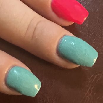 Top Nail - Teal nails didn't cure. - Close-up image of two fingers with freshly painted nails, one with red nail polish and the other with teal nail polish. The nails are glossy and appear neatly manicured. The fingers are resting on a brown surface, possibly leather or wood, with visible texture. The background includes a small part of a person's hand and a leather item. - Nail Salons Near Me - Cromwell, Connecticut