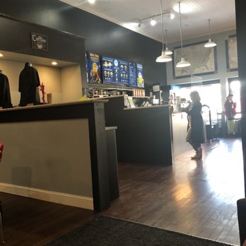 Aquamos Coffee Collaborative - Where it happens - A coffee shop interior featuring a counter with digital menu screens, pendant lighting, and customers waiting near the window. - Coffee & Tea Near Me - Waupaca, Wisconsin