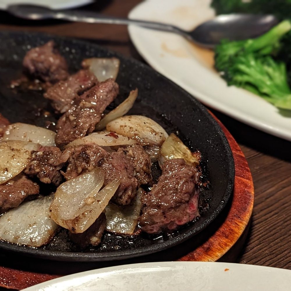 Basil Thai - Bo Lulac Cubed flank steak stir-fried with garlic, onions, butter, serving in a sizzling plate - Thai Near Me - La Quinta, California Basil Thai - Bo Lulac Cubed flank steak stir-fried with garlic, onions, butter, serving in a sizzling plate - Thai Near Me - La Quinta, California