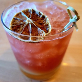 Standard Rec - Enter the dragon .  Unique flavor, getting use to. - A pink cocktail served in a clear glass, topped with a dried citrus slice and a decorative straw. The drink appears chilled with ice visible inside, and the background shows a wooden surface, suggesting a bar or restaurant setting. - Bars Near Me - Patchogue, New York