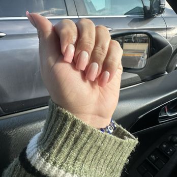 Opal Nails - The image shows a person's left hand with well-groomed, natural-colored nails, positioned inside a vehicle. The person is wearing a knitted sweater with green, white, and black stripes, and a bracelet with blue beads. Outside the vehicle, a parked silver or gray car is visible through the window, with the side mirror and part of the vehicle's body in view. - Nail Salons Near Me - Mount Prospect, Illinois