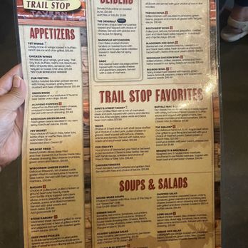 Trail Stop Tavern - Menu - Menu board from Trail Stop Tavern in Eagan, MN, displaying sections for appetizers, sliders, trail stop favorites, and soups & salads. The appetizers include wings, chicken wings, pub pretzel, onion rings, jalapeno poppers, and more. Slider options feature Nashville hot chicken, nashville hot chicken, and others. Trail stop favorites include dishes like Santi's street tacos, tacos, cod fish fry, chicken tenders, and buffalo mac & cheese. Soups & salads include house-made soups, dinner salad, classic Caesar, steak & bleu wedge, chopped salad, cobb salad, and wedge side salad. The board has a brick background with the restaurant's logo at the top left. - American Near Me - Eagan, Minnesota