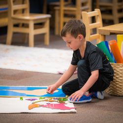 Childpeace Montessori School - A young student working with a wooden map on the floor.