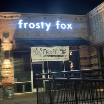Frosty Fox - Frosty Fox, a boba tea shop in Austin, TX, features illuminated signage and a banner advertising its offerings, with a brick exterior and outdoor railing. - Desserts Near Me - Austin, Texas