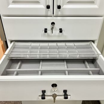 Classy Closets - A white storage drawer is pulled open, showing multiple empty compartments designed for organization. Inside, there is a clear plastic tray with several small sections, likely used for storing small items or accessories. The drawer is part of a larger white cabinet or furniture piece, situated in an indoor setting with other furniture visible nearby. - Cabinetry Near Me - Grapevine, Texas