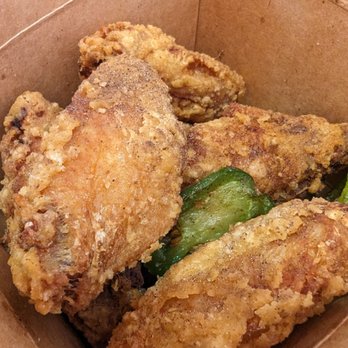 Cluck2Go - Salt & pepper wings 5/5 - The image shows several pieces of fried chicken with a crispy, golden-brown coating, accompanied by green peppers, inside a brown paper takeout container. The chicken appears to be seasoned and breaded, with a textured surface. - Singaporean Near Me - Pasadena, California