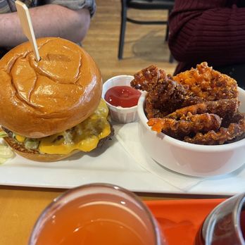 Claim 52 Kitchen - Smash burger and sweet potato fries - A cheeseburger with melted cheese, lettuce, and a bun is served with waffle fries and ketchup on a white tray. - Gastropubs Near Me - Eugene, Oregon