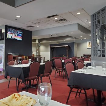 Saffron Restaurant - tables and chairs in a restaurant - A dining area with tables set for service, red chairs, a fireplace, and two mounted TVs showing sports, within a restaurant setting. - Indian Near Me - Bloomingdale, Illinois