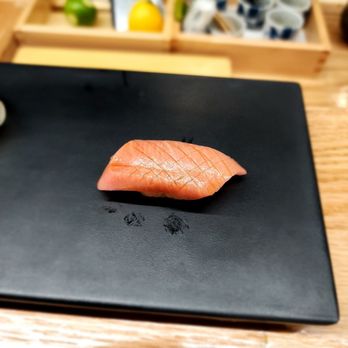 Kurama Omakase - a piece of salmon on a black plate - Sushi Bars Near Me - Keene, New Hampshire Kurama Omakase - a piece of salmon on a black plate - Sushi Bars Near Me - Keene, New Hampshire