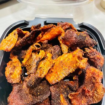 Cinder BBQ - Fried chicken skins - A black plastic takeout container filled with fried chicken skins, some with a crispy, dark exterior, and others showing the meat inside, with a clear plastic lid partially open. - Bars Near Me - Washington, DC, District of Columbia