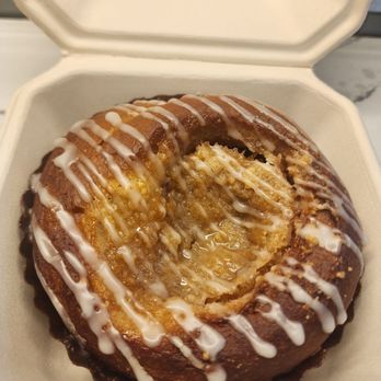 Breadhive Bakery & Cafe - Peach crumble bun - A peach crumble bun with icing drizzle is shown inside a bakery box, with a bite taken out of it, revealing the crumbly interior. - Cafes Near Me - Buffalo, New York