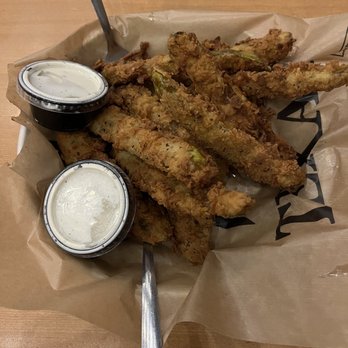 Circa 1880 - Fried pickle spears - Fried pickle spears are presented on a paper-lined tray with two cups of creamy dipping sauce, accompanied by metal utensils. - American Near Me - Baird, Texas